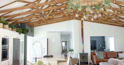 Bright rustic open-plan kitchen featuring exposed timber beams and hanging edison bulbs