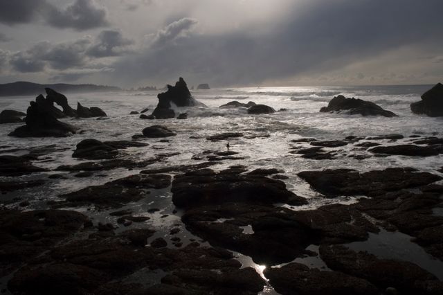 Dramatic seascape capturing rocky shore at twilight with ocean waves crashing against rocks. Dark sky with heavy, stormy clouds adds a moody atmosphere. Perfect for use in travel magazines, nature blogs, desktop wallpapers, and themed photo collections.