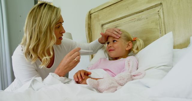 Mother caring for her young daughter in bed, checking temperature with thermometer. Suitable for concepts related to parenting, family healthcare, illness at home, and caring for sick children. Can be used in articles, blogs, advertisements related to health, parental guidance and childcare.