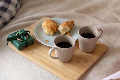 Romantic breakfast in bed with coffee, croissants and wrapped gift on bamboo serving board