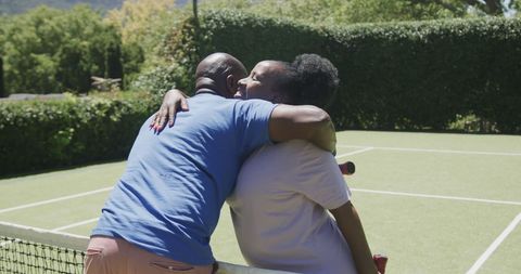 Happy senior couple embracing on sunny tennis court