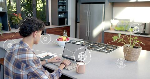 Young man typing on laptop at modern kitchen island for remote work with network overlays