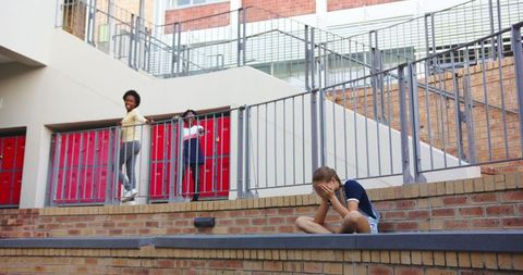 Child feeling upset near school buildings, students interacting