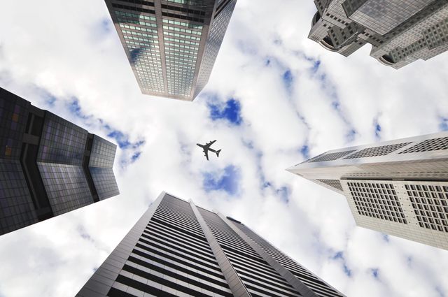 Low angle view of plane and tall buildings against blue sky. Travel and business concept