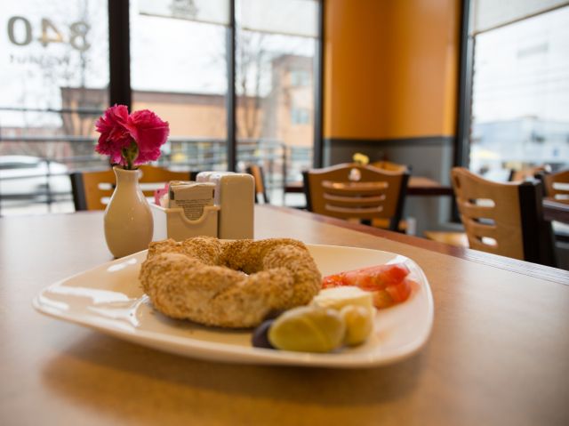 Bagel on white plate with fresh fruit in cozy cafe with patio view. Ideal for marketing dining experiences or casual cafe atmospheres. Suitable for food blogs, restaurant promotions, and menus.