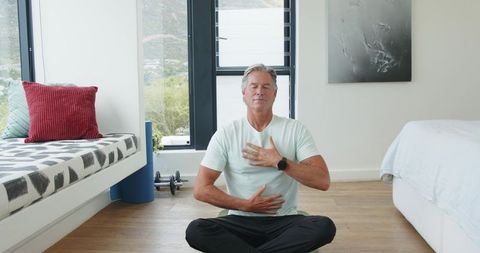 Middle-aged man practicing mindful breathing in bright minimal bedroom