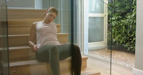 Young woman relaxing on wooden stairs with sunlight streaming through glass door