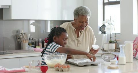 Grandmother teaching granddaughter baking in sunlit modern kitchen, multigenerational bond