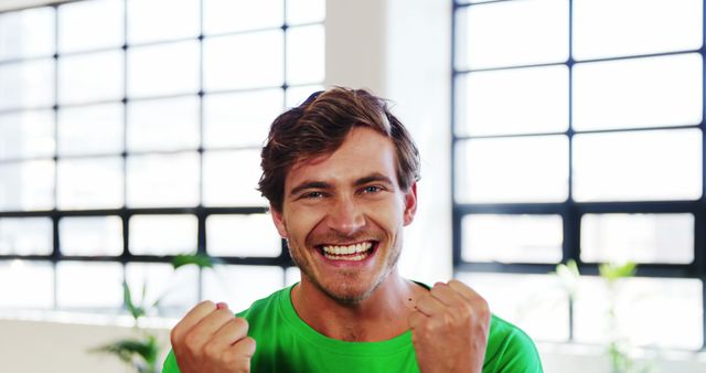 A young Caucasian man is celebrating with a joyful expression and clenched fists, with copy space. His bright smile and victorious gesture suggest a moment of personal achievement or good news.