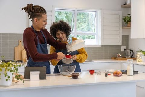 Couple baking together in bright modern kitchen, sifting flour at island