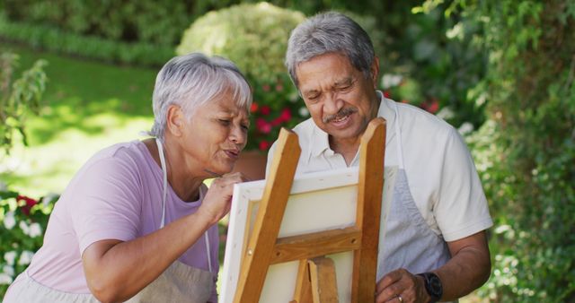Senior couple enjoying painting together in a sunny garden. The image captures a moment of connection and creativity, perfect for illustrating articles about retirement, aging, hobbies for senior citizens, well-being, and outdoor activities.
