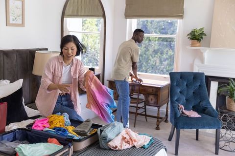 Diverse couple packing colorful summer clothes on bed preparing suitcase for trip