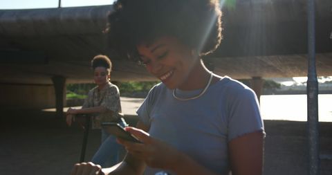 Biracial Twins Enjoying Smartphones While Riding Scooters in Park