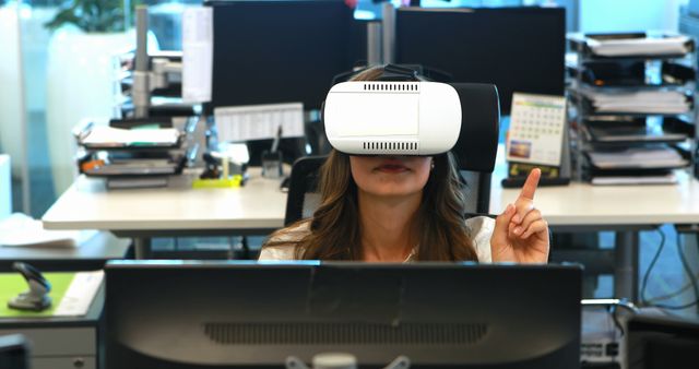 Businesswoman explores virtual reality using a VR headset in contemporary office. Potential uses include illustrating the integration of technology in modern workplaces, employee training, or presentations on VR in business. Captures themes of innovation, advancement, and future trends.