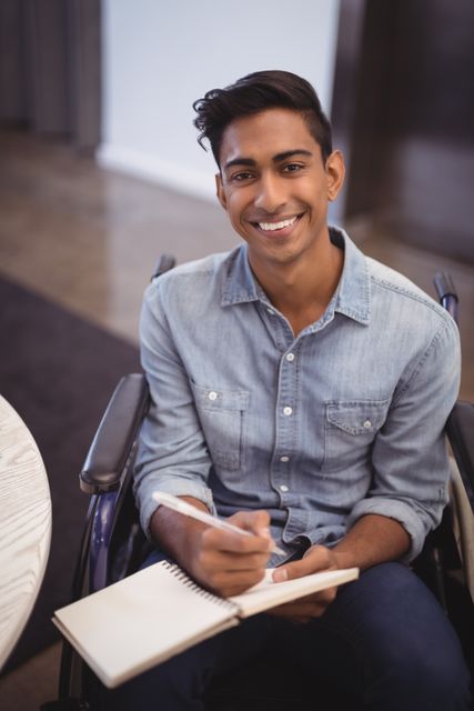 Portrait of smiling businessman writing in book while sitting on wheelchair