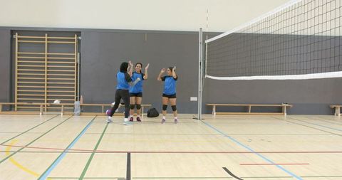 Diverse female volleyball teammates gathering and celebrating near net on school indoor court