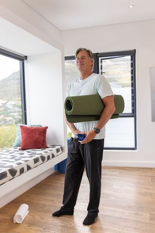 Mature man carrying rolled yoga mat and water bottle in bright minimalist home
