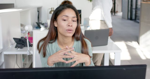 Young businesswoman engaged in a conference call sitting at desk in a modern office. Ideal for corporate communication materials, remote work or teamwork themes in blogs and presentations, and diversity or professional environment projects.