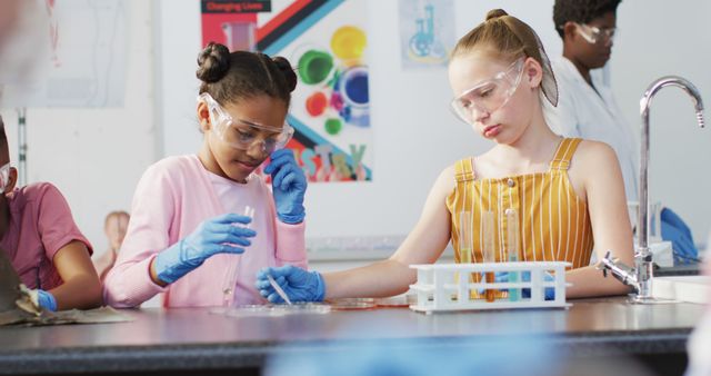 Two diverse female students wearing safety goggles and working together while conducting a science experiment in a school laboratory. They are handling lab equipment and materials, demonstrating teamwork and collaboration. Ideal for use in educational websites, school promotional materials, or articles about STEM education and classroom activities.