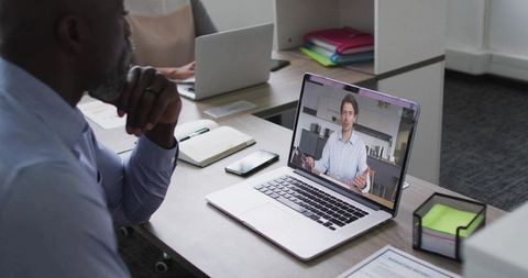 Business professional watching virtual presentation on laptop in modern coworking office