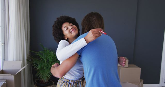 Couple embracing with joy in their new home with moving boxes visible in background. Useful for themes of relocation, new beginnings, family life, and teamwork.
