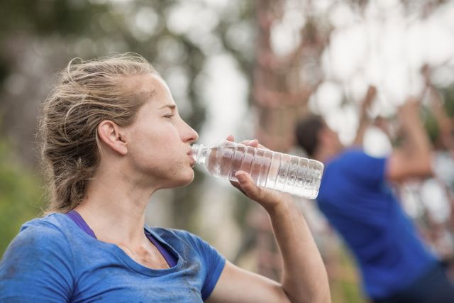 Woman drinking water from bottle during obstacle course in boot camp
