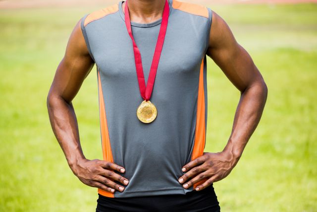Athlete standing outdoors with hands on hips, showcasing gold medal around neck. Ideal for use in sports-related content, motivational materials, fitness promotions, and articles on athletic achievements.