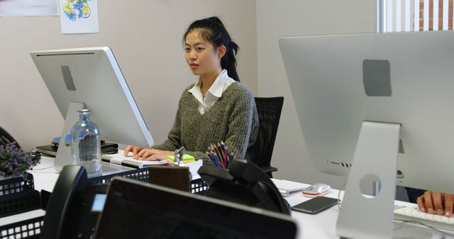 Asian woman working on computer in a modern office. Suitable for illustrating professional work environments, office settings, employee productivity, tech usage, and business processes.