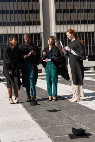 Diverse female graduates celebrating on urban rooftop wearing gowns holding diplomas
