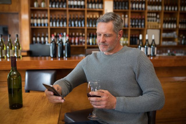 Smiling senior man using mobile phone while having red wine in restaurant
