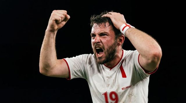 Shouting soccer player raising fist and holding head wearing number 19 england wristband