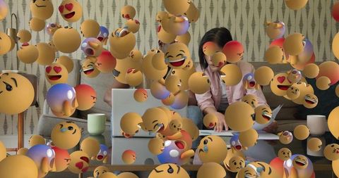 Remote working korean woman typing on laptop surrounded by floating emoji reactions
