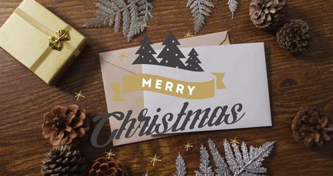 Merry christmas card lying on rustic wood table with gold present, pinecones, silver fern