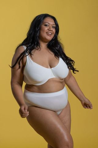 Confident indian plus size model smiling and posing in white lingerie on yellow backdrop