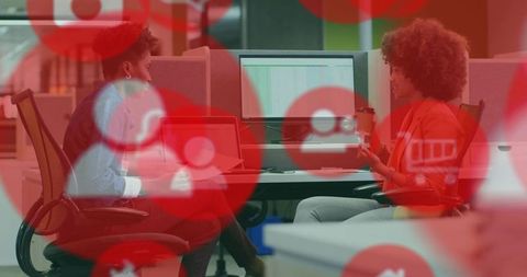 Two women collaborating at open-plan office workstation with red ui overlays