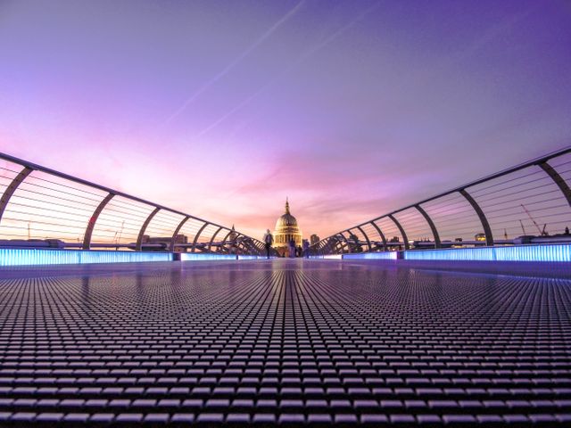 This image captures afootbridge with modern design leading towards a historic cathedral during a vibrant sunset. The scene is excellent for use in travel blogs, tourism promotions, city guides, and architectural websites showcasing blending old and new architectural styles. It highlights the serene yet dynamic character of urban landscapes at twilight, making it ideal for marketing city experiences.