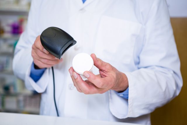 Pharmacist scanning medicine container with barcode scanner in pharmacy. Useful for illustrating topics related to healthcare, pharmacy operations, medication management, and the use of technology in healthcare settings.