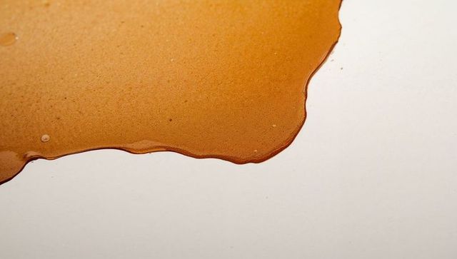 Spreading caramel syrup pooling on white surface with glossy amber texture close-up macro