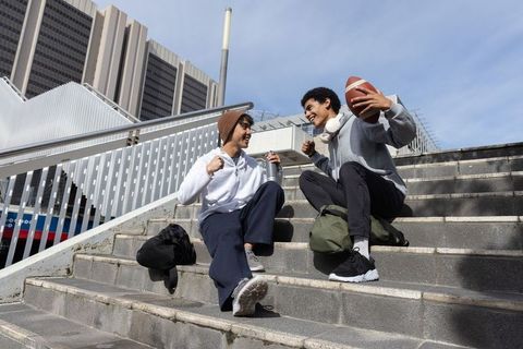 Diverse male teenagers cheering while holding football and water bottle on urban steps