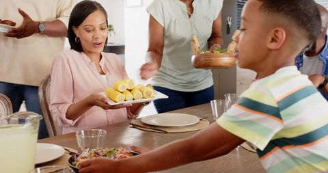 Multigenerational family passing dishes, sharing corn on cob, enjoying warm mealtime