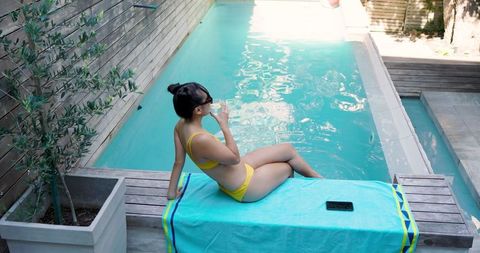 Woman Relaxing by Poolside Enjoying Refreshing Drink in Sunny Outdoor Setting