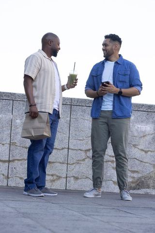 African american friends chatting on urban plaza holding smoothie and smartphone