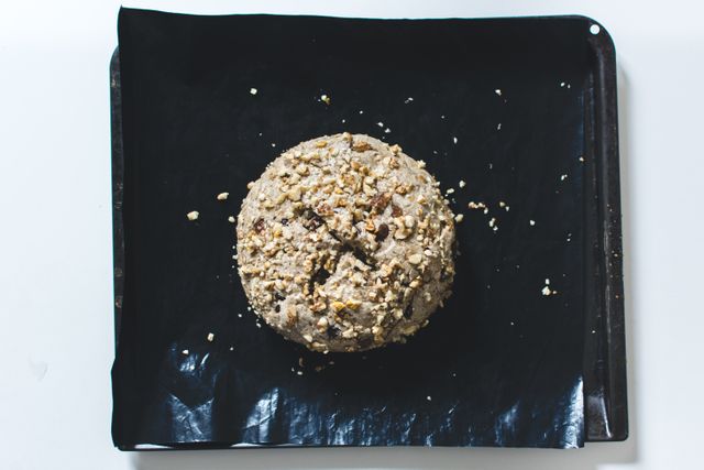 Freshly baked round wholegrain bread with a sprinkle of nuts on top placed on a black tray. Ideal for use in culinary articles, healthy eating blogs, bakery advertisements, or cookbooks showcasing artisan bread and home baking.