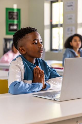 African american boy focusing on laptop with hands pressed in calm classroom moment