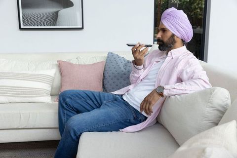 Mid adult man using voice command on smartphone relaxing at home