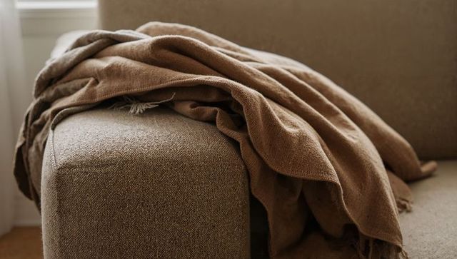 Neutral living room throw draping over beige sofa arm with textured weave and tassels