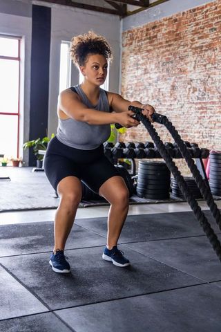 African american woman performing battle rope workout in industrial gym boosting strength