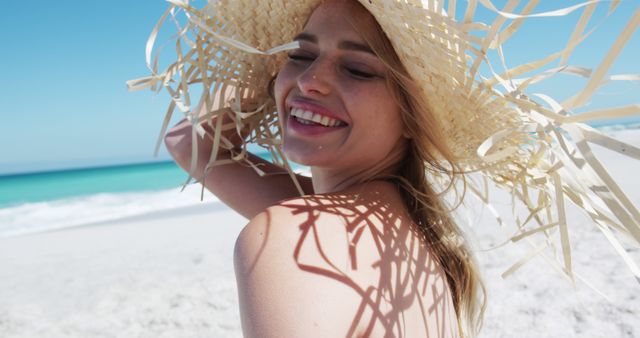 This image features a cheerful woman wearing a sunhat and relaxing on a sunny, sandy beach with the ocean in the background. It is ideal for promoting summer vacations, beach destinations, travel agencies, and lifestyle blogs focused on travel and relaxation.