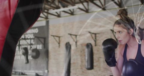 Focused Female Boxer Training with Punching Bag at Gym