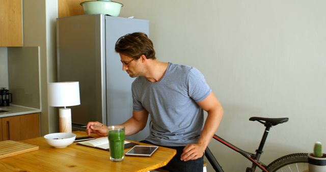 Young man working on notes while eating breakfast at kitchen counter - Download Free Stock Images Pikwizard.com